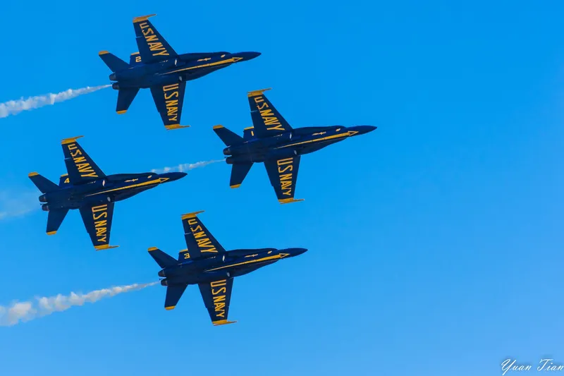 Four Blue Angels jets flying in tight diamond formation with smoke trails