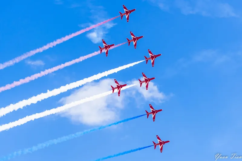 Seven Red Arrows jets climbing in formation, trailing red, white, and blue smoke